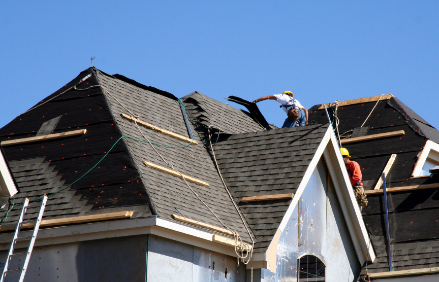 Construction workers putting shingles on the roof of a house.